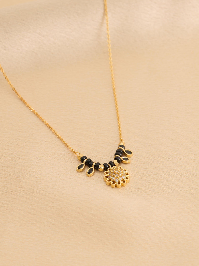 Gold necklace with black and gold floral pendants on a beige background