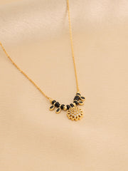 Gold necklace with black and gold floral pendants on a beige background