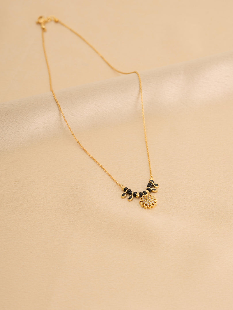 Gold necklace with black and gold pendants on a beige background