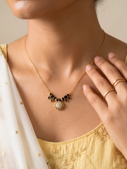 Gold necklace with black beads worn by a person in a yellow top.