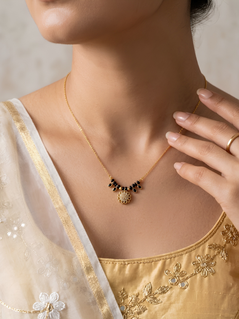 Close-up of a person wearing a gold necklace with a pendant, set against a neutral background.