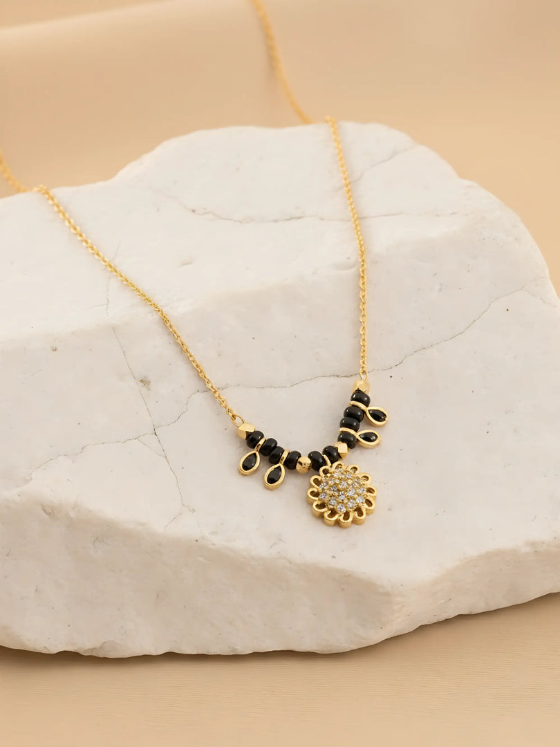 Gold necklace with black and gold pendants on a white stone surface