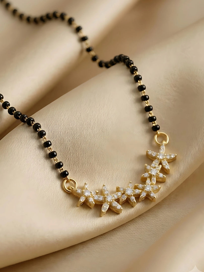 A close-up of a gold and black beaded necklace with a curved gold pendant adorned with clear crystals, displayed on draped beige satin fabric.