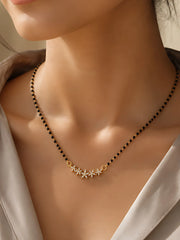 A close-up of a woman's neck and chest wearing a delicate black beaded necklace with a gold-toned centerpiece featuring small star and crescent moon charms.