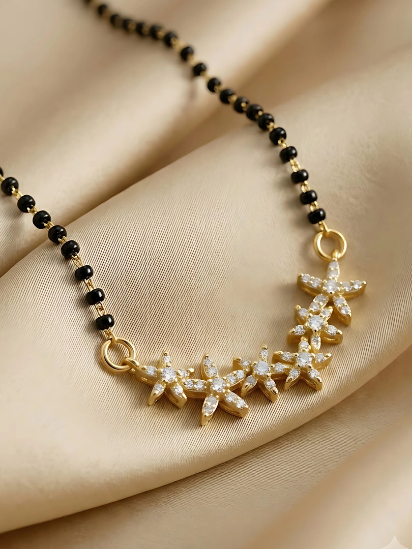A gold-toned necklace with a crescent moon-shaped pendant adorned with clear crystals, paired with a black beaded chain and small gold spacer beads, displayed on draped beige satin fabric.