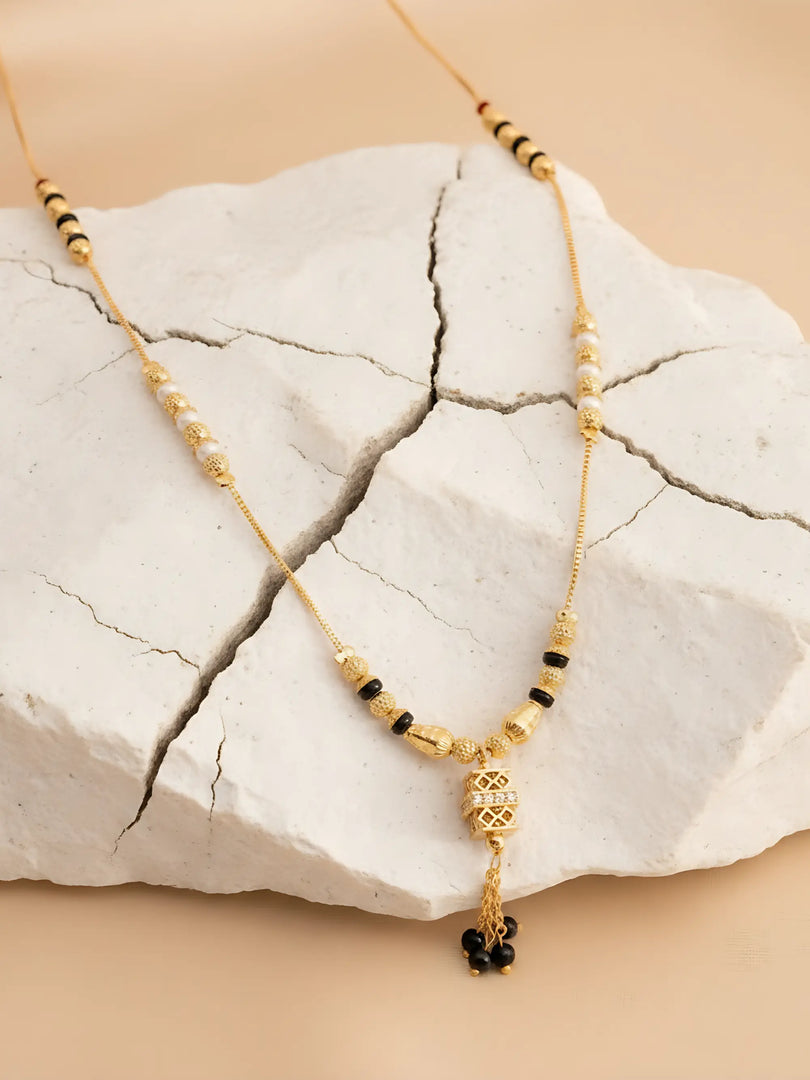 Gold necklace with black beads on a textured white stone surface